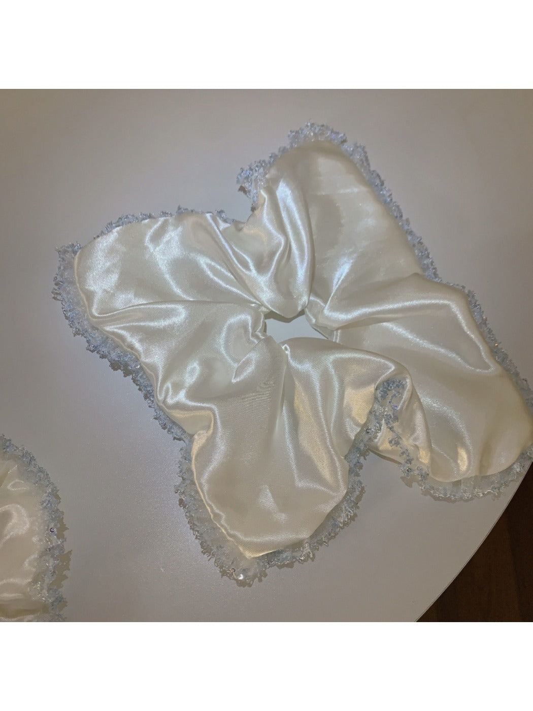 Satin white lace trim scrunchie packaged in a clear plastic bag with branding