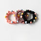Hand holding multiple colorful beaded hair ties showing their stretch and texture