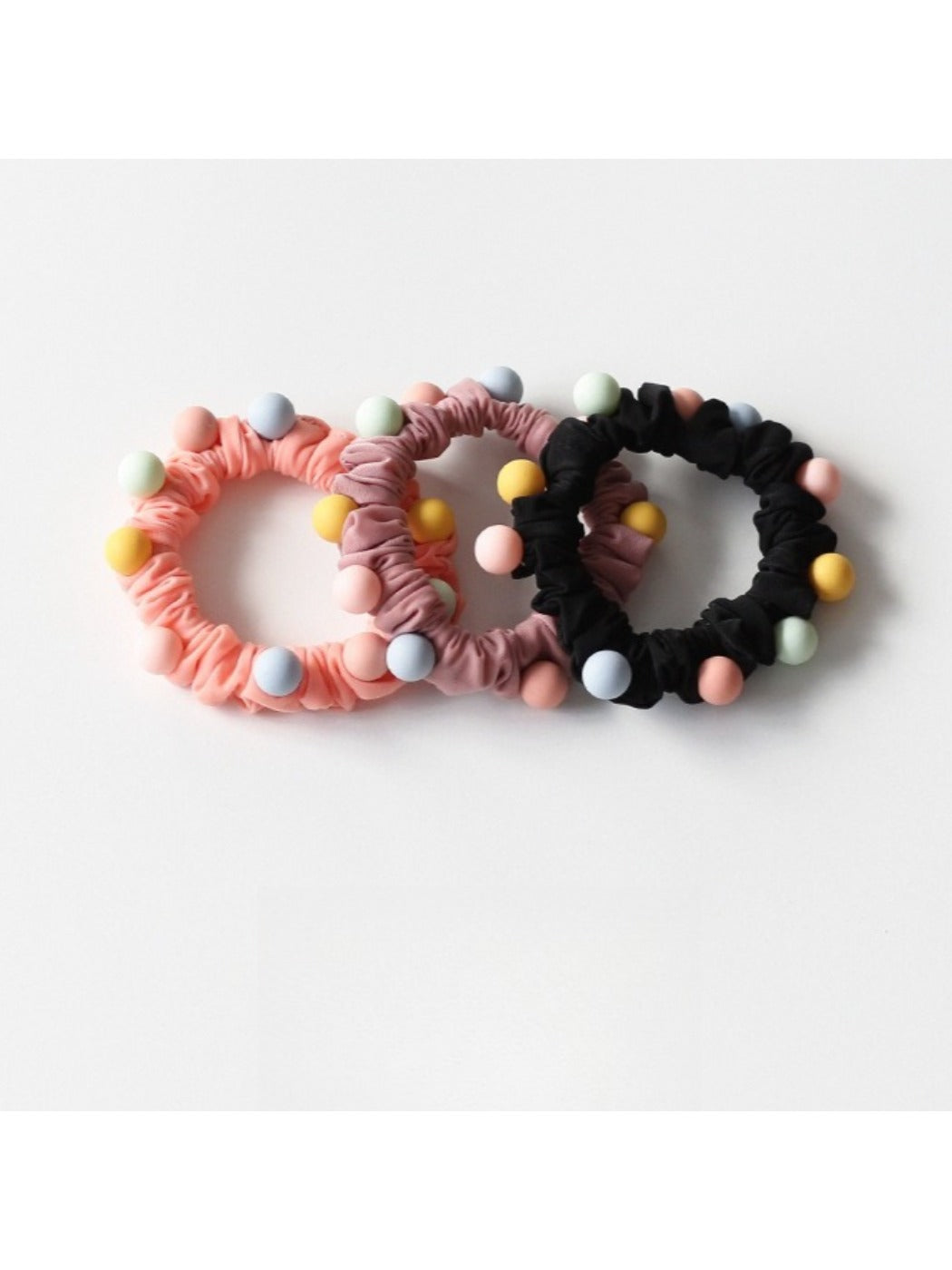 Hand holding multiple colorful beaded hair ties showing their stretch and texture