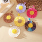 Close-up of a single raffia sunflower-shaped earring with yellow petals and a brown center
