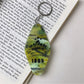 Diamond-shaped pendant keychain displayed on a wooden surface with natural light