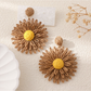 Pair of colorful floral raffia statement earrings on a neutral fabric background