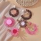 Pair of pink and black raffia woven earrings displayed on white background