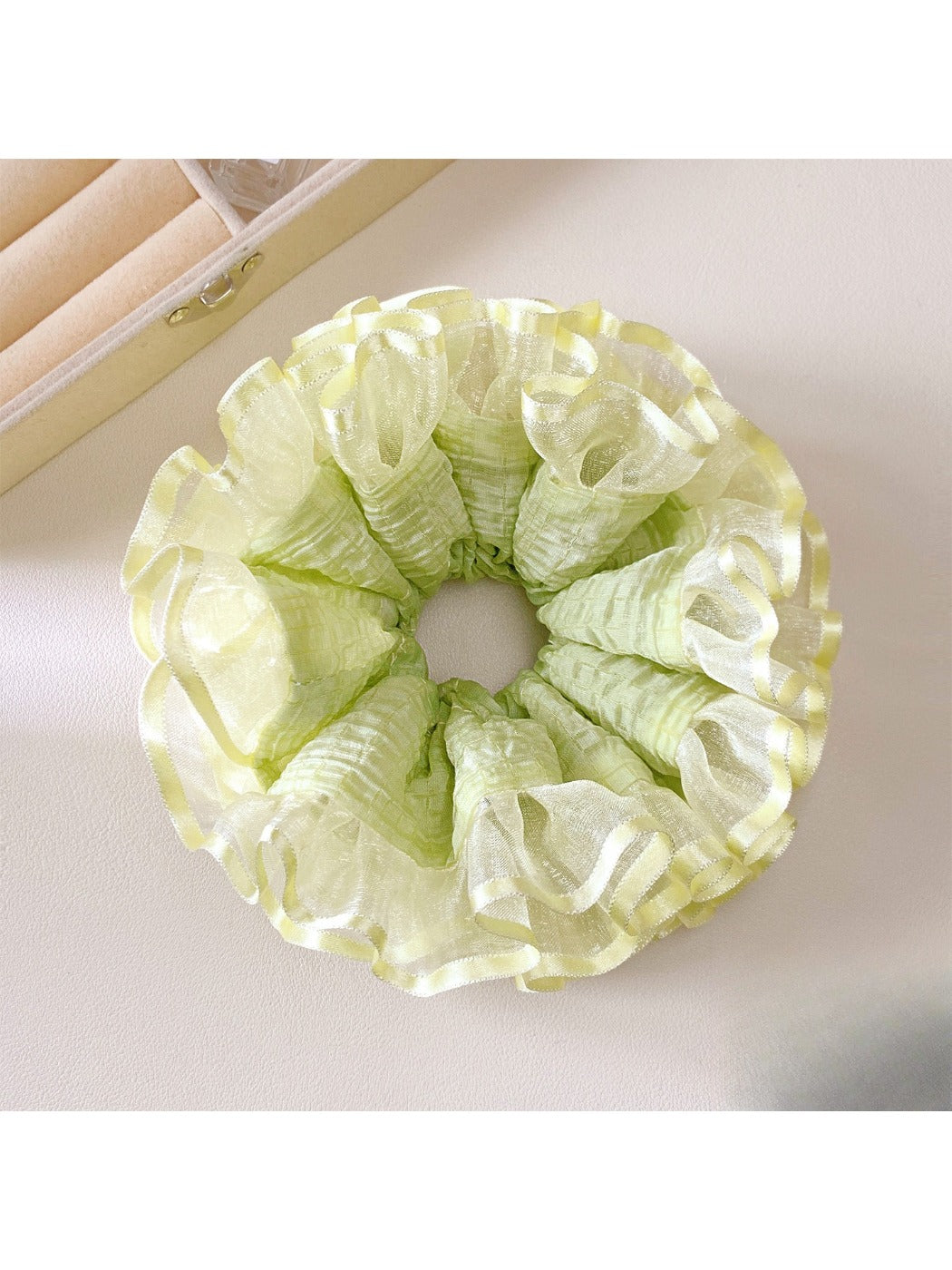 Light green fabric scrunchie with ruffle detailing on a white background