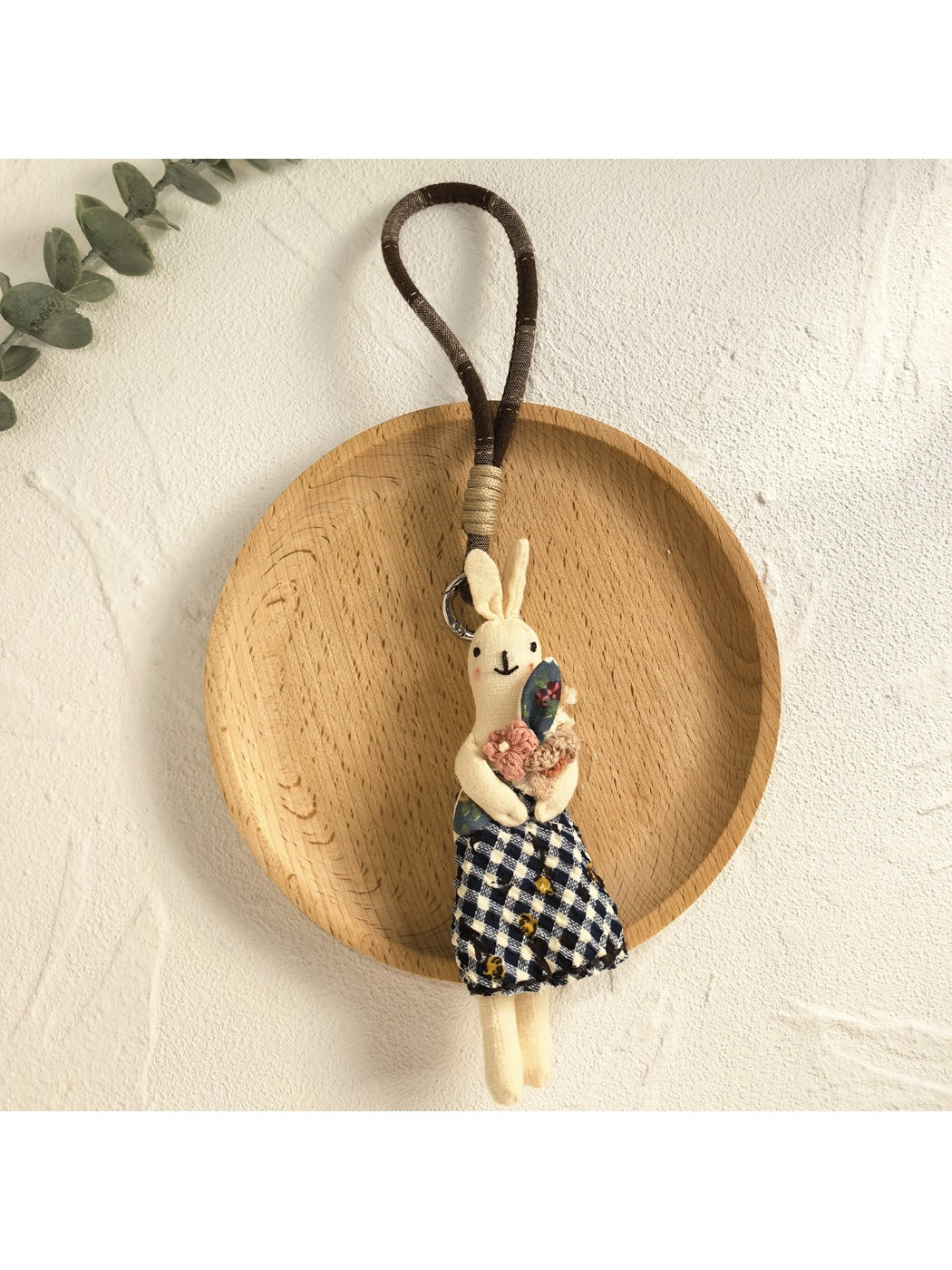 Minimalist bunny keychain next to a small plant on a wooden surface