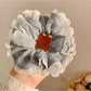 Gray ruffle scrunchie wrapped around a ponytail on a model with dark hair