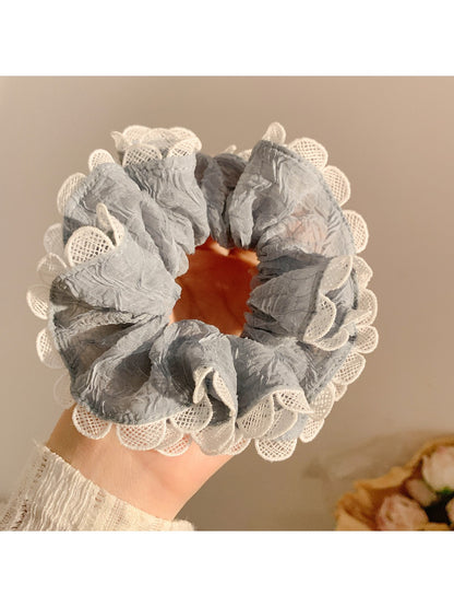 Gray ruffle scrunchie wrapped around a ponytail on a model with dark hair