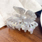 Beau butterfly hair claw clip in pastel pink placed on a wooden surface
