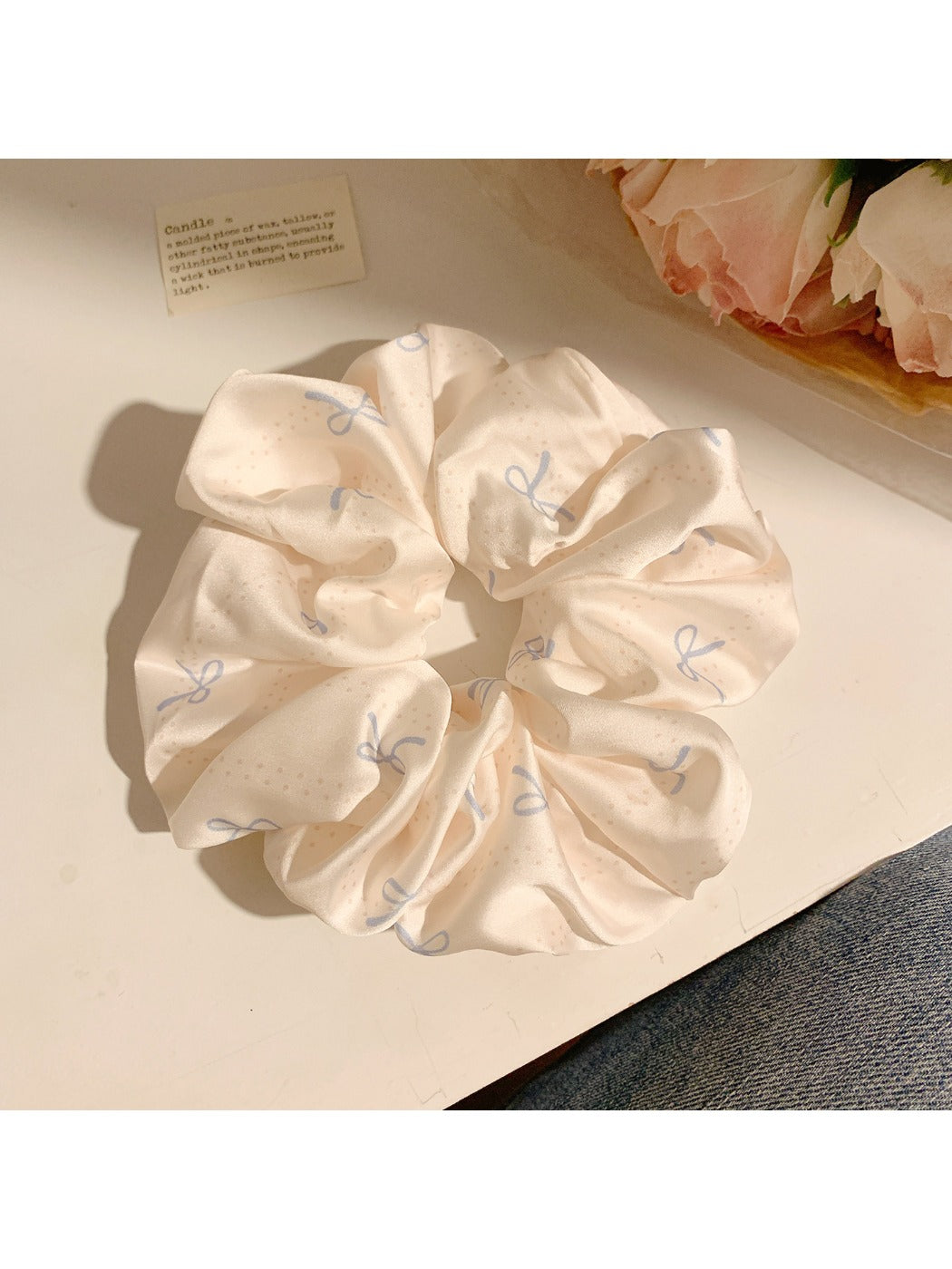Flat lay of minimalist satin scrunchie with bow pattern on neutral surface