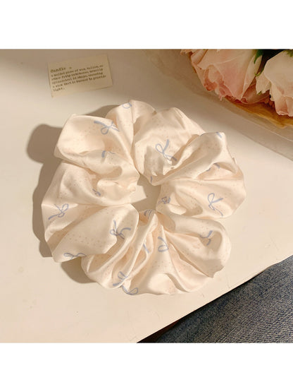 Flat lay of minimalist satin scrunchie with bow pattern on neutral surface