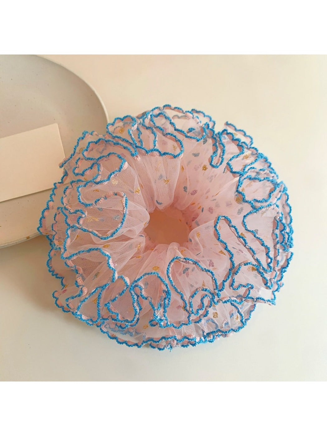Pink ruffled scrunchie styled on a wrist with layered fabric design