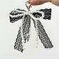 Lace bow keychain hanging from a handbag strap in natural lighting