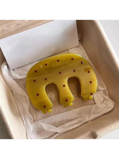 Yellow Beau claw hair clip with white polka dots on a white background