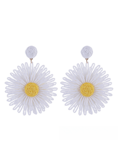 Colorful floral raffia earrings placed next to green leaves for styling