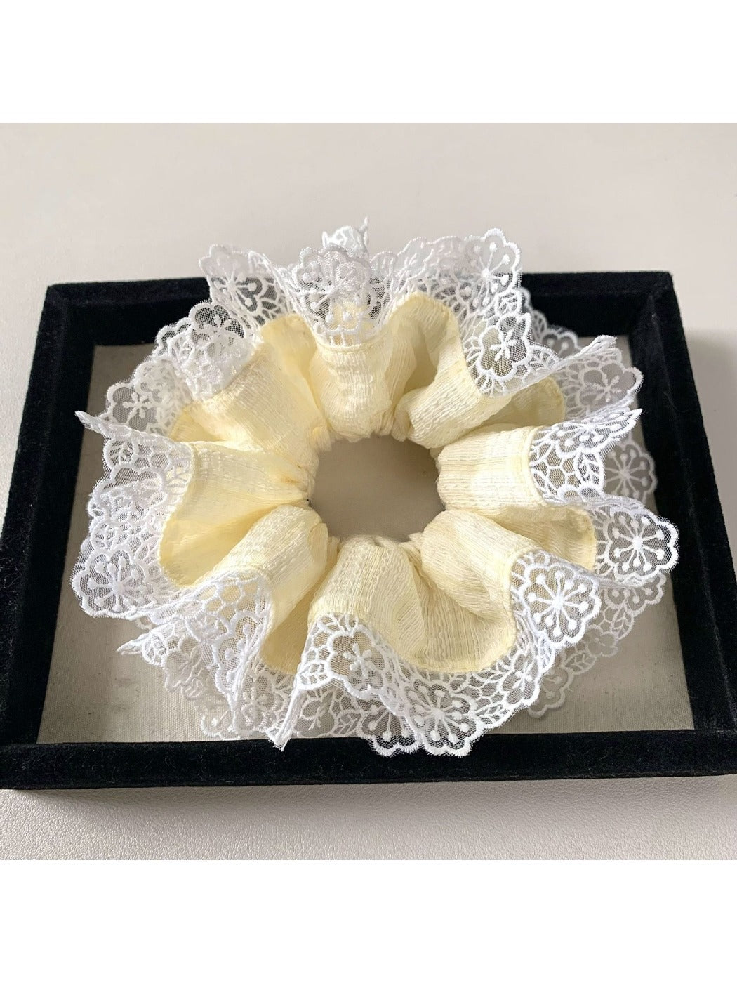 Yellow and white fabric hair scrunchie displayed flat on a wooden surface