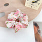 Gifty scrunchie held in hand, showing size and delicate floral ruffled fabric with bow