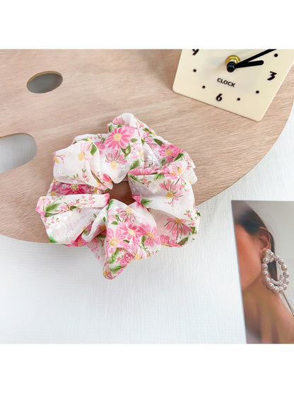 Gifty scrunchie held in hand, showing size and delicate floral ruffled fabric with bow