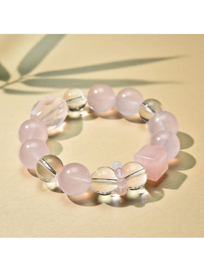 Pink beaded bracelet with gold details laid flat on a textured surface