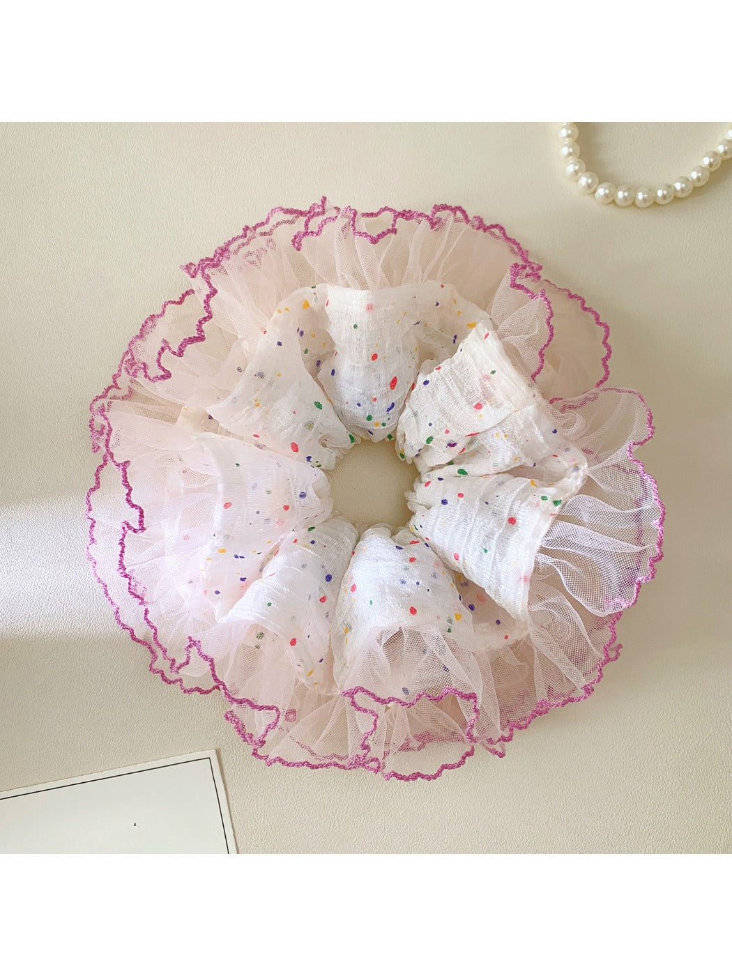 Scrunchie with vibrant polka dots and ruffled edges displayed flat