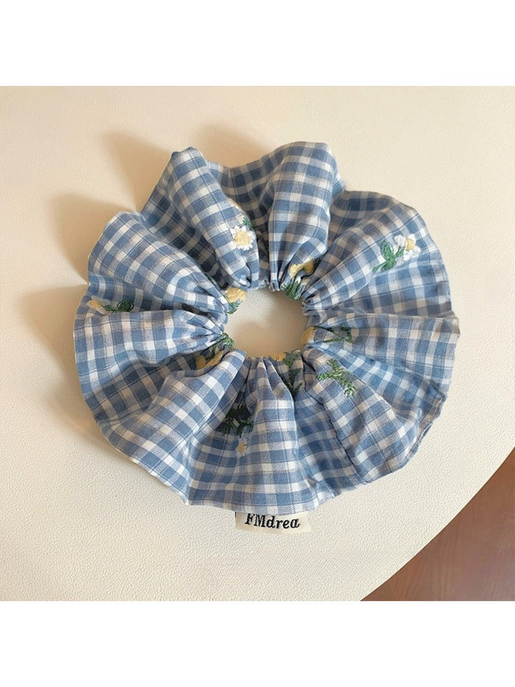 Blue plaid scrunchie with embroidered flower held in hand against neutral background