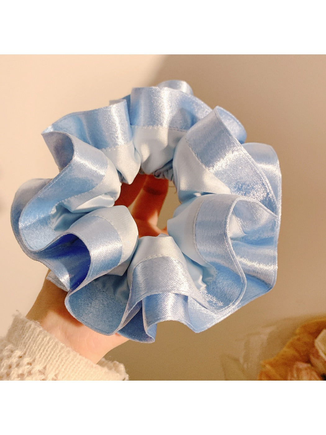 Model holding Gifty satin ruffle scrunchie with manicured nails, showcasing size