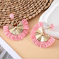 Earedge raffia fan earrings placed on a natural fabric surface