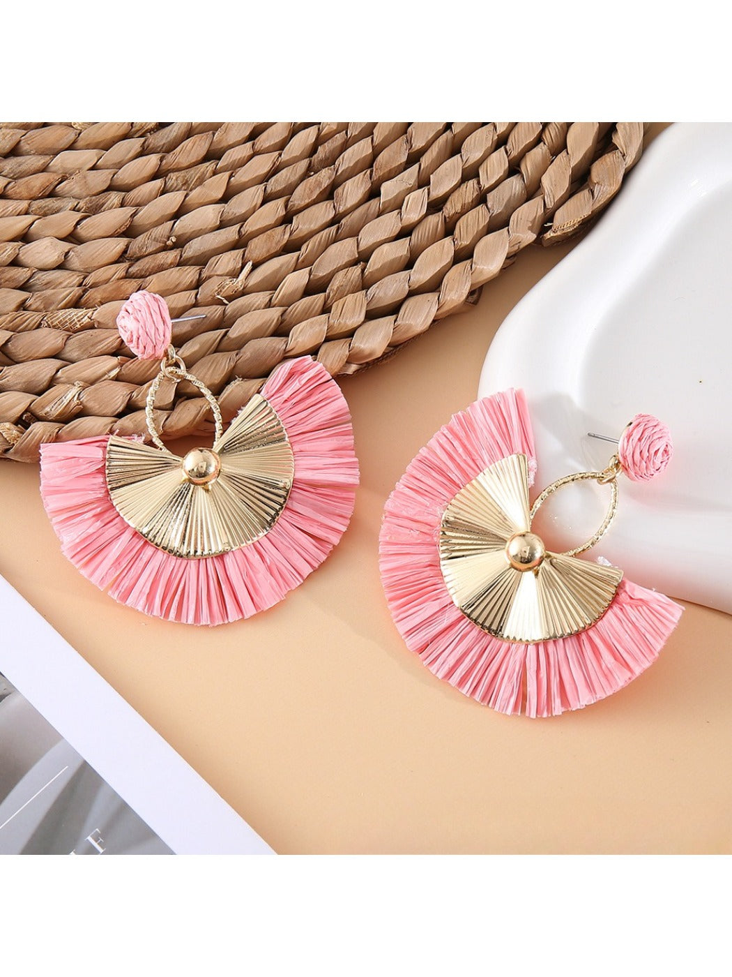 Earedge raffia fan earrings placed on a natural fabric surface
