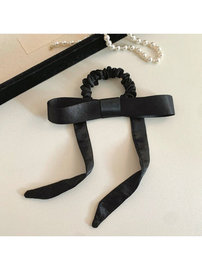 Top view of a satin bow hair tie showing the elastic band and bow detail