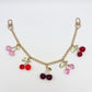 Cherry charm dangling from a gold chain on a white fabric background
