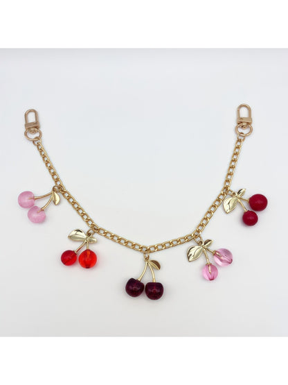 Cherry charm dangling from a gold chain on a white fabric background