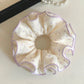 Purple scrunchie with white polka dots displayed on a wooden surface