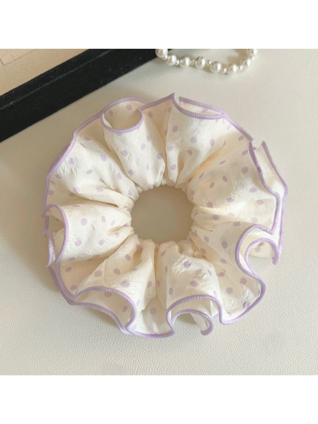 Purple scrunchie with white polka dots displayed on a wooden surface
