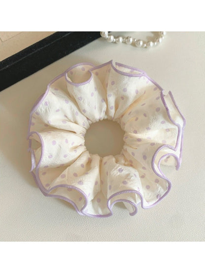 Purple scrunchie with white polka dots displayed on a wooden surface