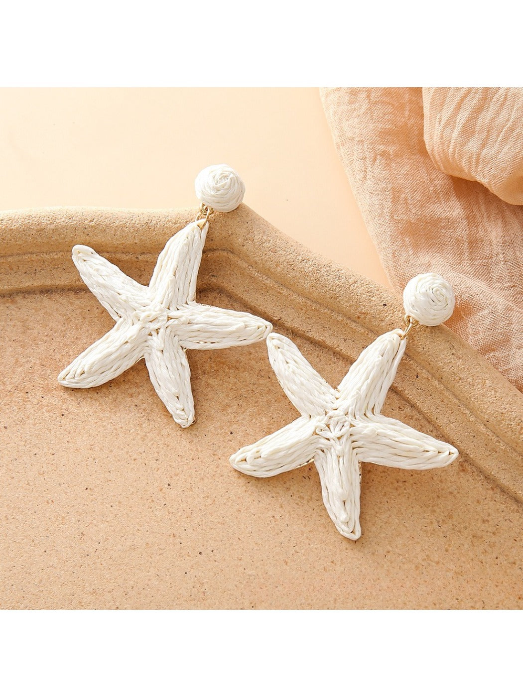 Starfish drop earrings displayed with beach-themed props