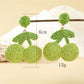 Side view of raffia cherry earrings showing woven texture and green leaf detail