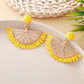 Pair of raffia fan shaped drop earrings displayed on wooden surface