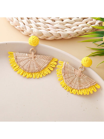 Pair of raffia fan shaped drop earrings displayed on wooden surface