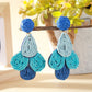 Earedge raffia drop earrings hanging from a white jewelry holder against a neutral background