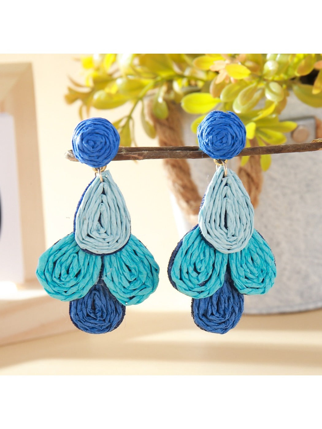 Earedge raffia drop earrings hanging from a white jewelry holder against a neutral background