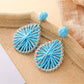 Pair of natural raffia teardrop earrings displayed against a neutral fabric background