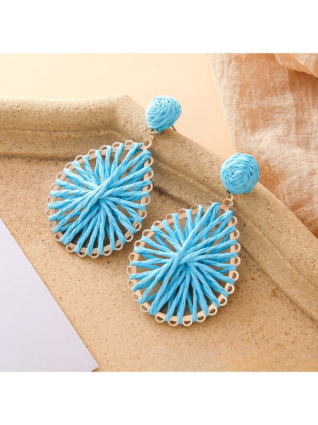 Pair of natural raffia teardrop earrings displayed against a neutral fabric background