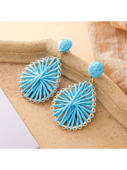 Pair of natural raffia teardrop earrings displayed against a neutral fabric background