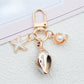 Gold conch shell keychain displayed on a reflective black surface