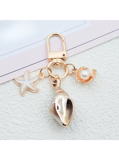 Gold conch shell keychain displayed on a reflective black surface