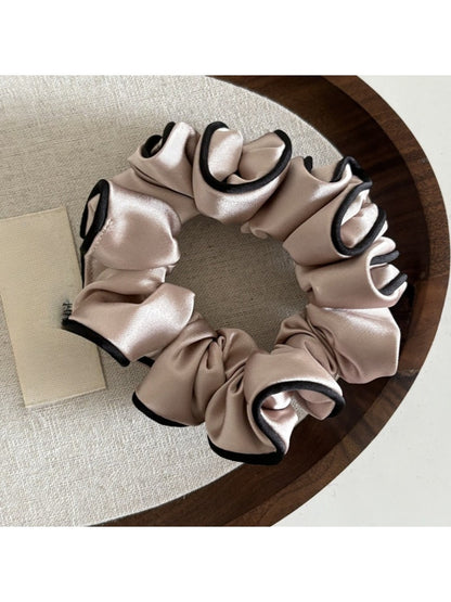 Gifty satin scrunchie in pink shown alongside other hair accessories on a table