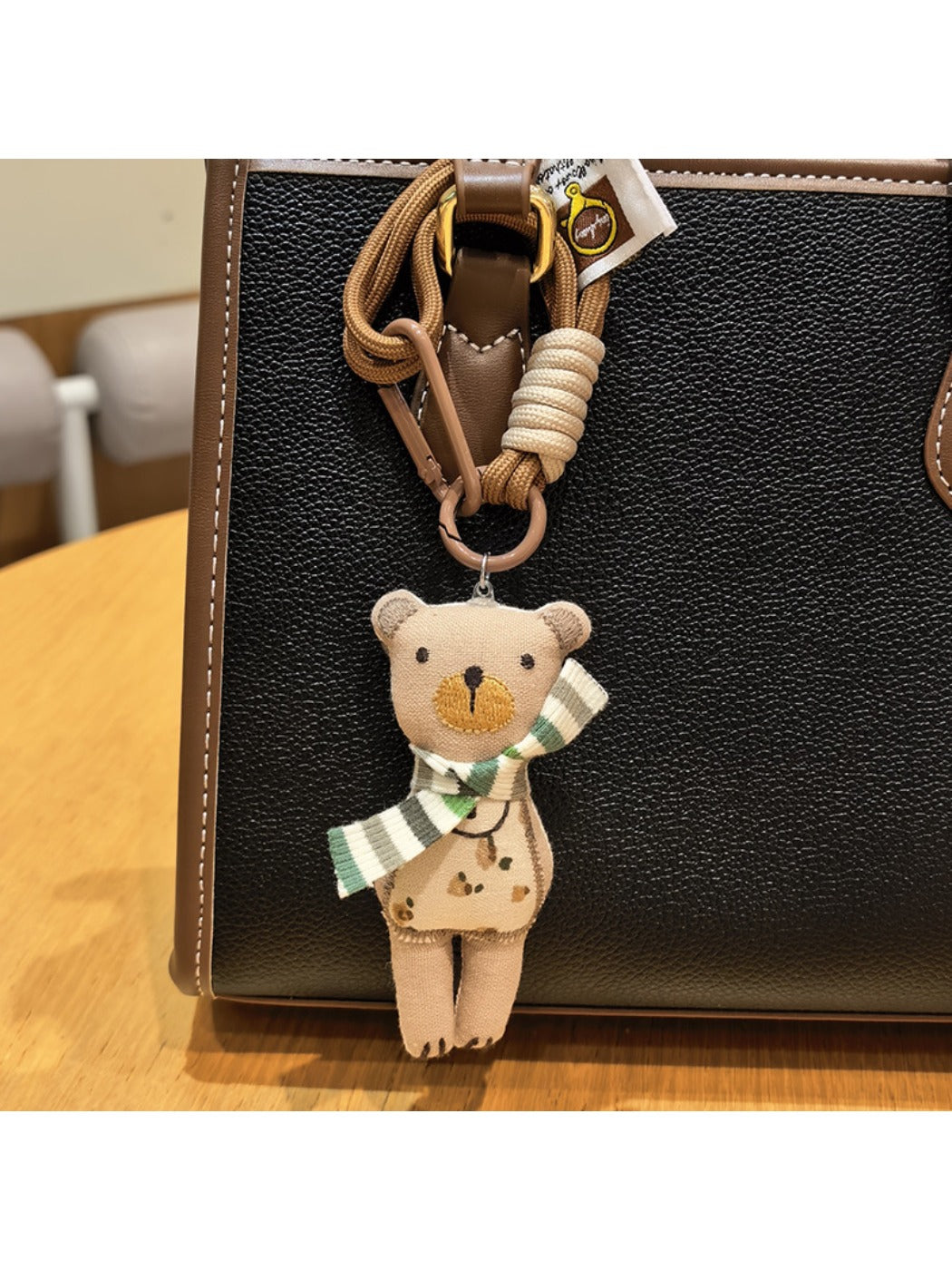 Fabric bear cub keychain attached to a brown leather bag strap