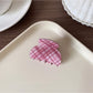 Beau hair claw clip with pink plaid pattern next to matching accessories