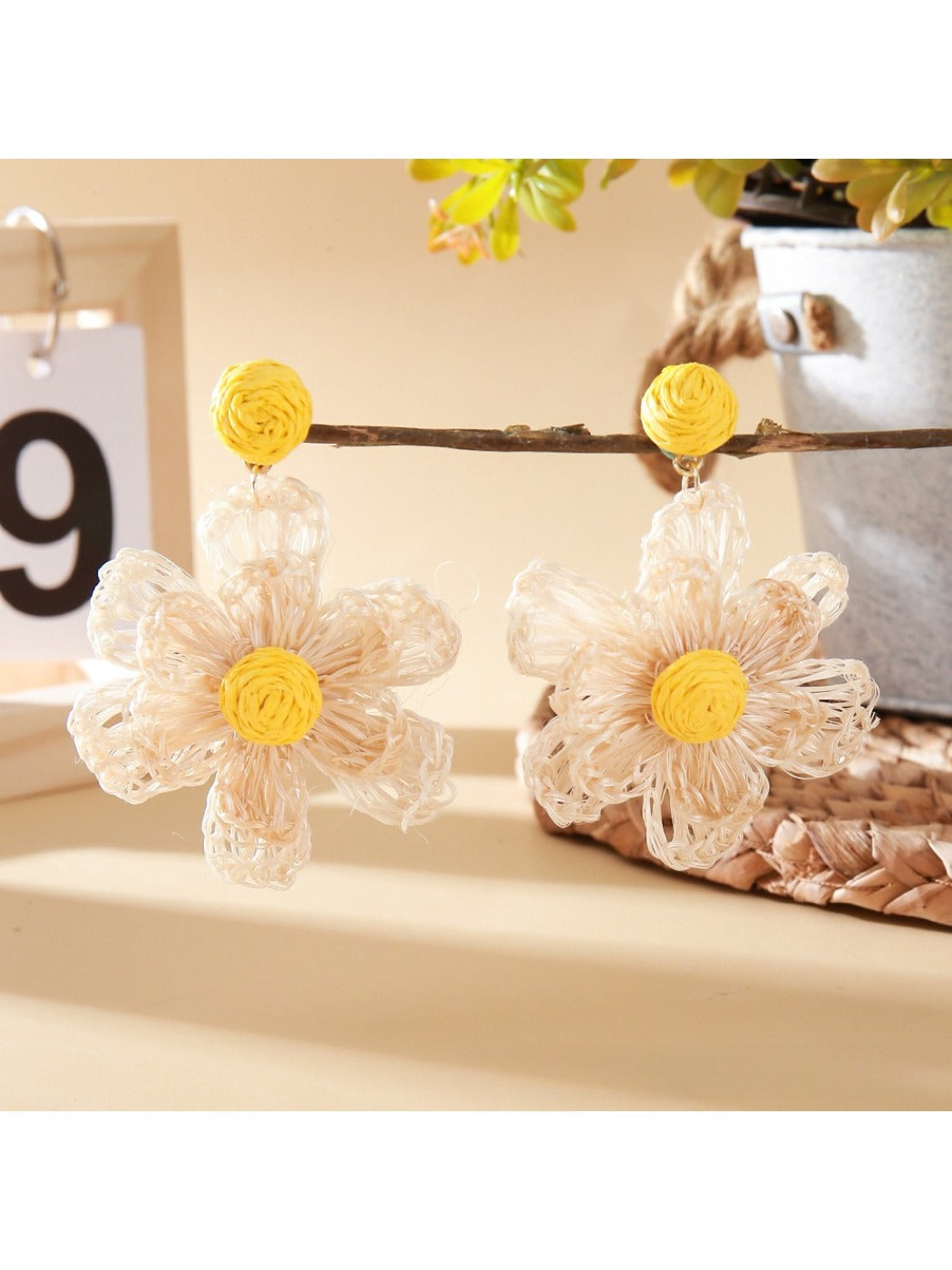 Pair of raffia flower drop earrings hanging from a jewelry stand