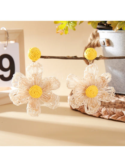 Pair of raffia flower drop earrings hanging from a jewelry stand