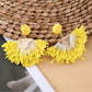 Earedge fan-shaped raffia earrings hanging from a jewelry stand